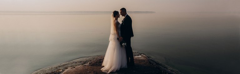 The dynamic duo of a bride and groom standing by a lake, looking into each other's eyes.