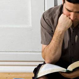 A seated man leaning over an open Bible with studious look about him as he reads and ponders what it means to find your identity in Christ