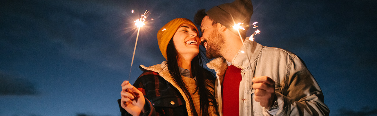 Smiling couple embracing while holding sparklers and sharing prayers for New Year