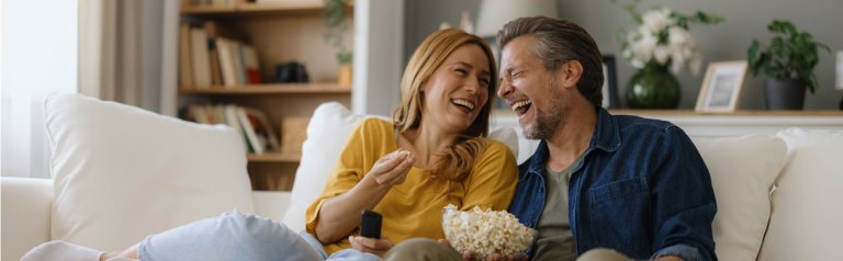 A mature husband and wife intentionally encourage more joy in marriage as they relax for a fun evening of sharing some laughs and a bowl of popcorn in their home.