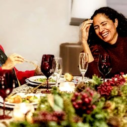 A multigenerational stepfamily gathers around a beautifully decorated dining table set with lots of holiday food, where they enjoy laughter along with their holiday dinner.