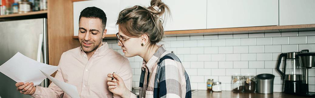 A married couple standing in their kitchen looking at bills and discussing finances.