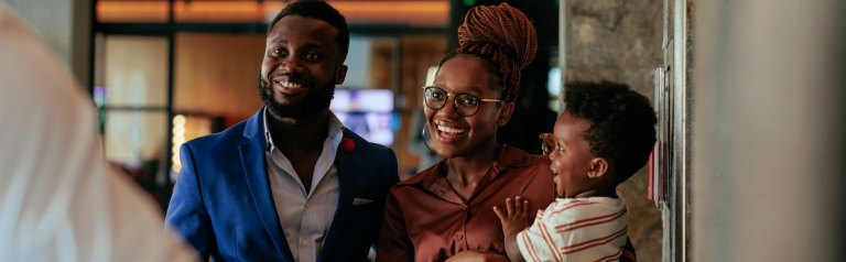 A happy, smiling husband with his wife, who is carrying their smiling toddler, both greet a pastor, as they hope to find a church for their young family.