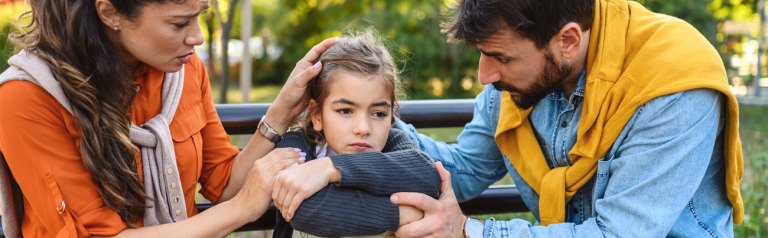 On a bench in a park a mother and father comfort their child when the world feels unsafe