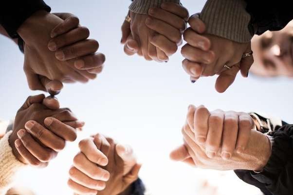 Adult hands of mixed races being held in a prayer circle.