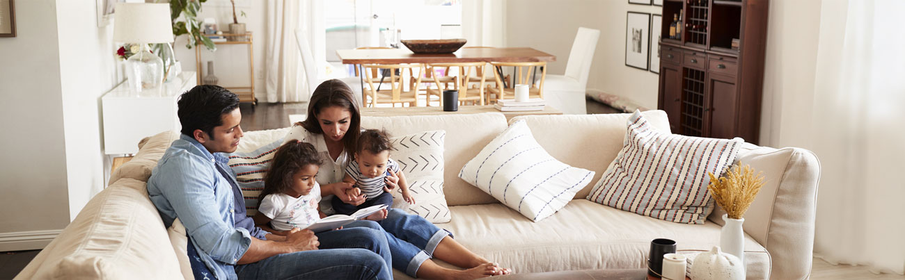 Young married couple seated comfortably on their living room sofa alongside their two children while leading a family Bible study to encourage their spiritual growth