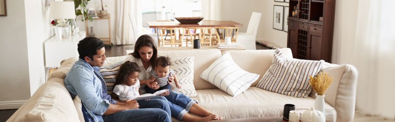 Young married couple seated comfortably on their living room sofa alongside their two children while leading a family Bible study to encourage their spiritual growth