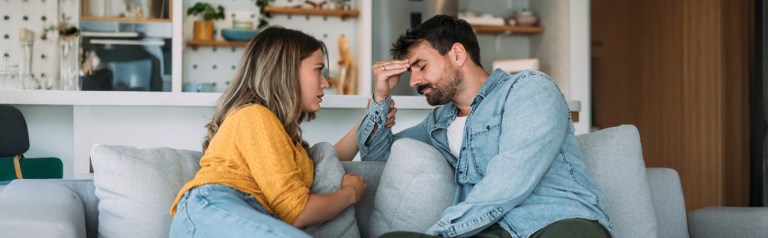 A couple seated opposite each other on their sofa display concern and dismay in their facial expressions while struggling with emotional safety in marriage