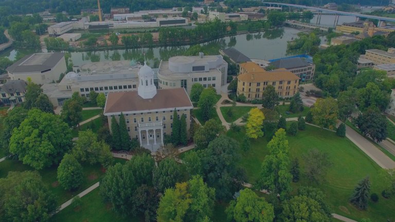 An aerial view looking down on lush green trees, grasses, and sidewalks surrounding downtown riverside area buildings of the city of Appleton, Wisconsin, a location of FamilyLife's Weekend to Remember® marriage retreat event.