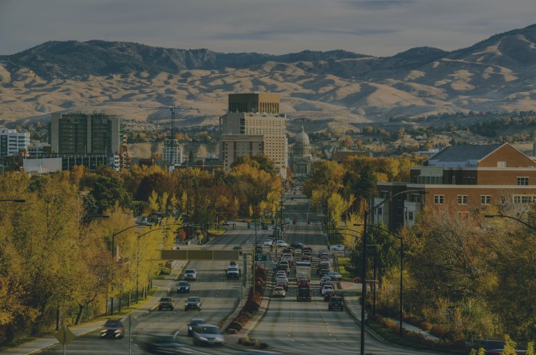 A long angle view showing off a tree-lined road with golden autumn leaves that leads into the city, and the rolling Boise Foothills serve as a backdrop to the downtown area of Boise, Idaho, a location of FamilyLife's Weekend to Remember® marriage retreat event.