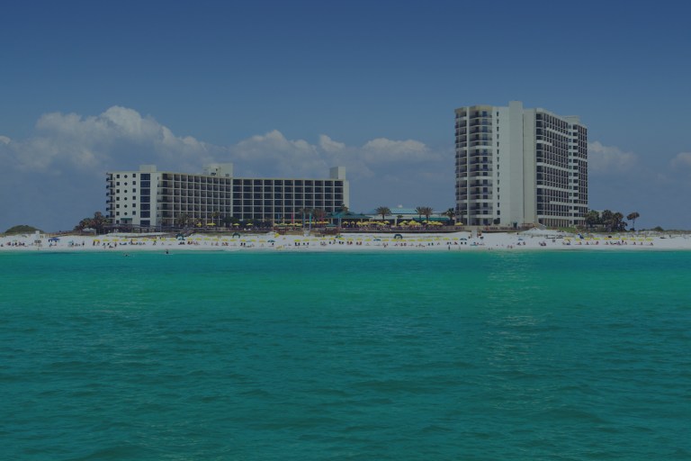 An offshore ocean view over teal waters looking back toward the white sandy beach lined with beach-goers and tall ocean-view buildings in Destin, Florida, a location of FamilyLife's Weekend to Remember® marriage retreat event.