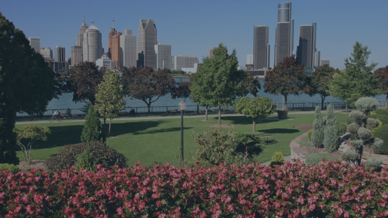 The eye-pleasing landscape design of a highly-manicured city park that overlooks a section of the beautiful Detroit Riverwalk set alongside the Detroit River, and rising in the background is the downtown city skyline of Detroit, Michigan, a location of FamilyLife's Weekend to Remember® marriage retreat event.