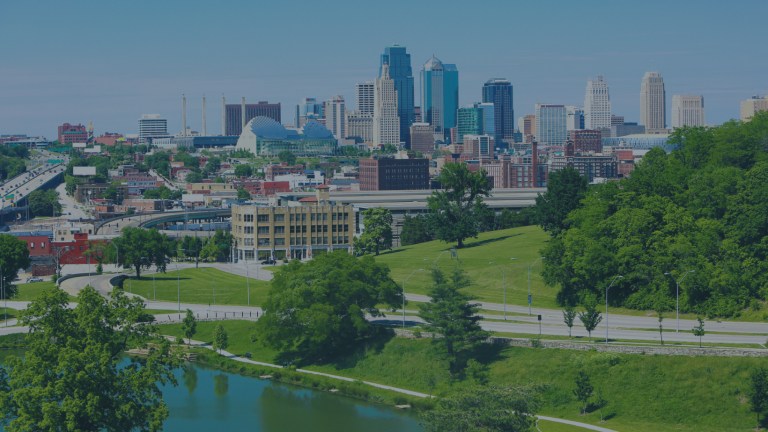 A wildlife pond with nearby walking trails and city park in the foreground, and a view toward the cityscape skyline in the background, all highlighted with the clear blue skies behind Kansas City, Kansas, a location of FamilyLife's Weekend to Remember® marriage retreat event.