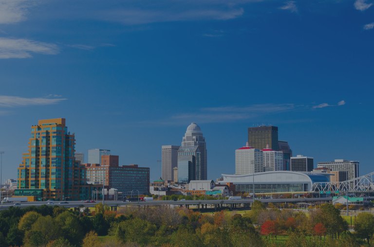 A beautiful, blue-sky view toward the cityscape skyline overlooking a tree-filled park and an elevated expressway crossing in front of downtown Louisville, Kentucky, a location of FamilyLife's Weekend to Remember® marriage retreat event.