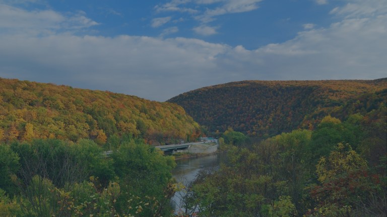 A view across colorful tree-covered mountains and valleys with a highway winding alongside a lake in the Poconos, Pennsylvania, a location of FamilyLife's Weekend to Remember® marriage retreat event.