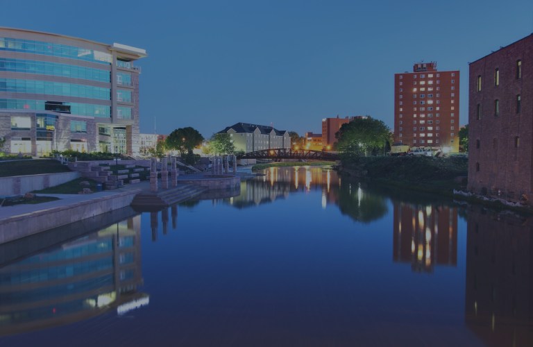 An early morning view that overlooks a still water section of the Big Sioux River flowing through downtown, which mirrors on its surface the lights and beautiful city buildings of Sioux Falls, South Dakota, a location of FamilyLife's Weekend to Remember® marriage retreat event.