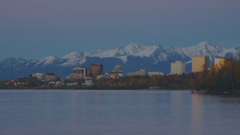 A view over the waters of Cook Inlet toward the tall city skyline of the downtown area with the backdrop of the Chugach Mountains all highlighting the city of Anchorage, Alaska, a location of FamilyLife's Weekend to Remember® marriage retreat event.