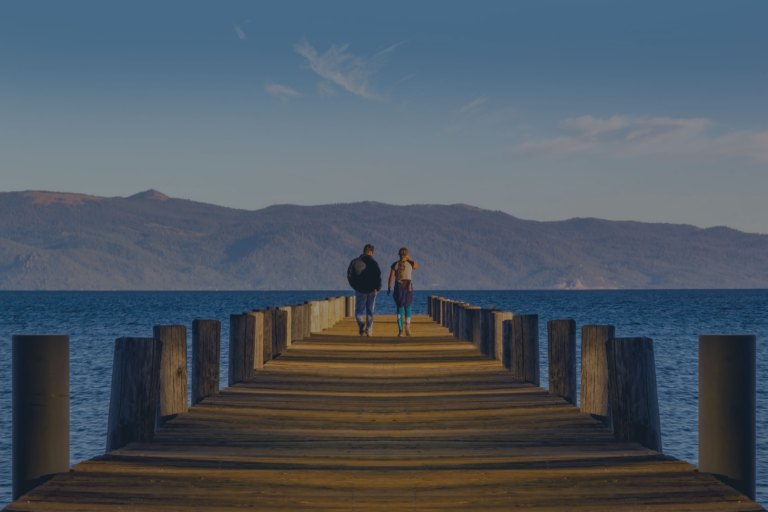 As they look toward the mountains in the distance, a married couple stand at the end of a long pier that extends out over Lake Tahoe, Nevada, one of the locations for FamilyLife's Weekend to Remember® marriage retreat.