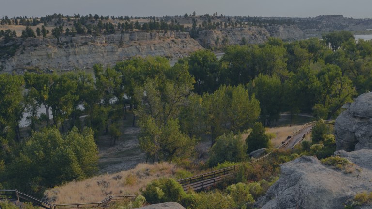 An aerial view of sandstone rimrocks featuring a wooden hiking trail nestled within the hillside rocks far above the river and near Billings, Montana, a location of FamilyLife's Weekend to Remember® marriage retreat event.
