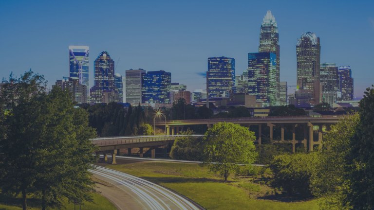 A city skyline view overlooking a lovely city park with a walking path, grassy areas, and lush green-leaf trees in Charlotte, North Carolina, a location of FamilyLife's Weekend to Remember® marriage retreat event.