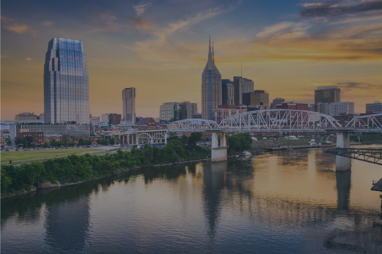 A beautiful riverside skyline view with tall city buildings and a bridge over the waterway, featuring a blue sky backdrop with large, sun-lit yellow swirling clouds highlighting downtown Nashville, Tennessee, a location of FamilyLife's Weekend to Remember® marriage retreat event.
