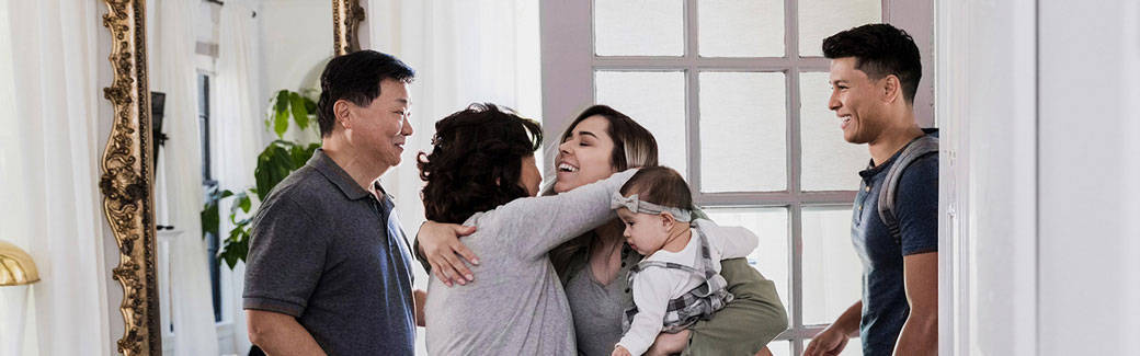 adult daughter, holding baby, hugging her mother while her father and husband look on.