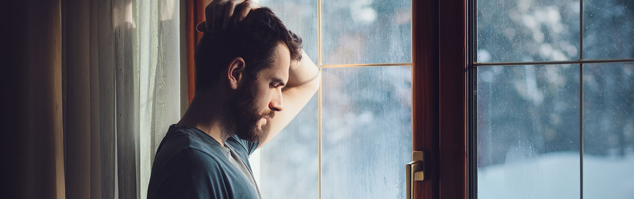 Man in front of a window, eyes downcast in thought